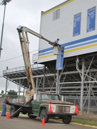 Roy Lister and Ken Swisher place new signs on the west side of the press box last week.